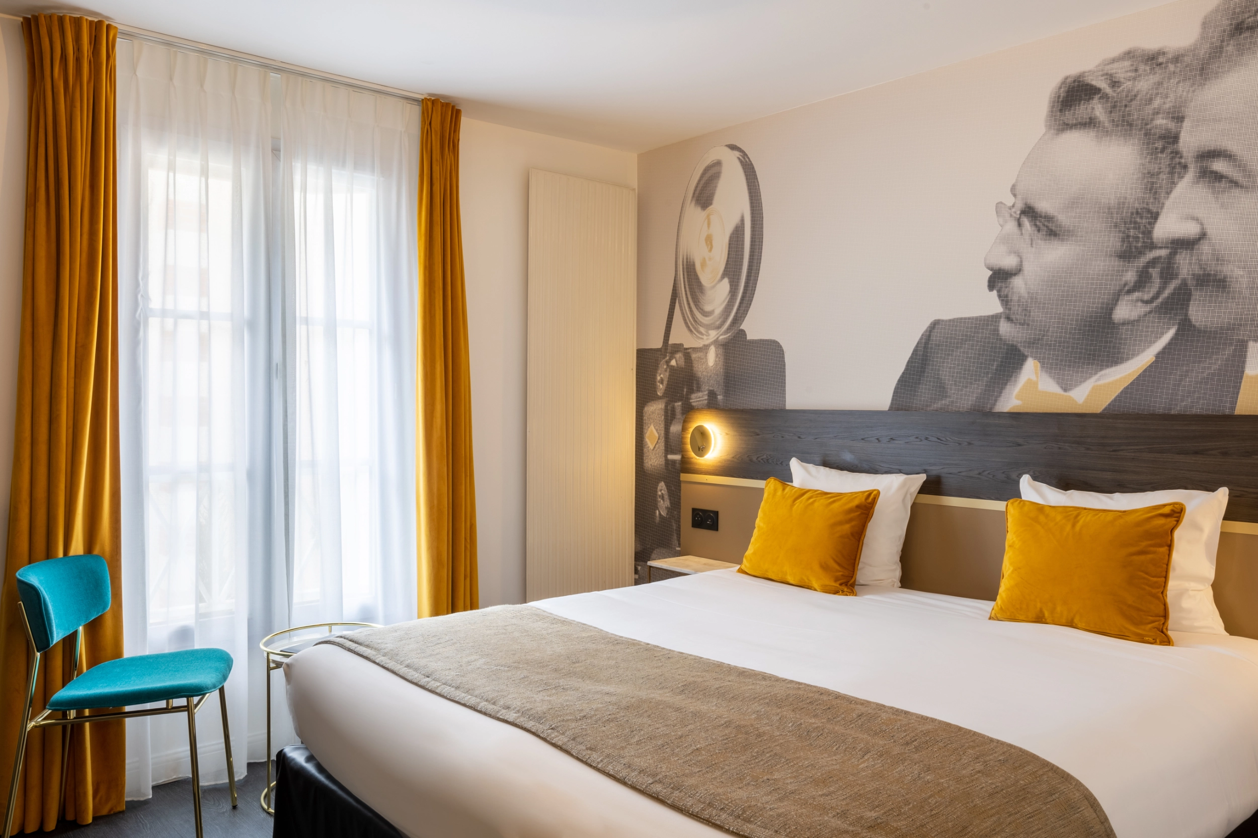 Soon Architecture - Une chambre d'hôtel moderne conçue par Soon architecture comprend un grand lit avec une literie blanche, des murs jaunes et blancs, un bureau professionnel avec une chaise et une lampe, des rideaux jusqu'au sol et une fenêtre laissant entrer la lumière naturelle.